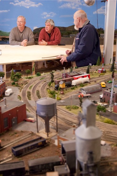 Kishwaukee Valley & Eakin Creek Model Railroad Club HO Gauge Assistant Superintendents (left to right) Al Price, N.27, Ron Butzen, N.17, and Bill Ed- dis, N.21, discuss plans for additions to the HO gauge model railroad empire in club’s home beneath Mill- grove Woodshop. (Photo by Chris LaPelusa/Sun Day)