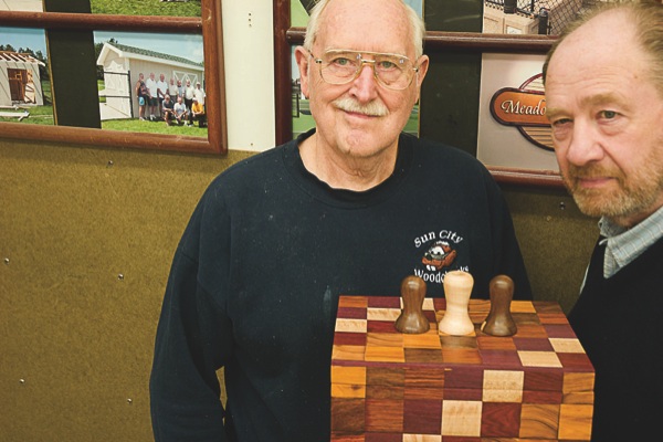 After puzzling over it, Woodchucks Bert Stohs (left) and Don Keene turned a box of puzzles and parlor games into a puzzle itself, operated by the three knobs seen on the box top. (Photo by Chris LaPelusa/Sun Day)