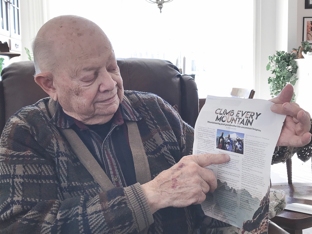 F. Schrauth displays an article featuring his daughter’s mother-in-law, who began climbing mountains when she was 90 years old. (Photo by Chris LaPelusa/Sun Day)